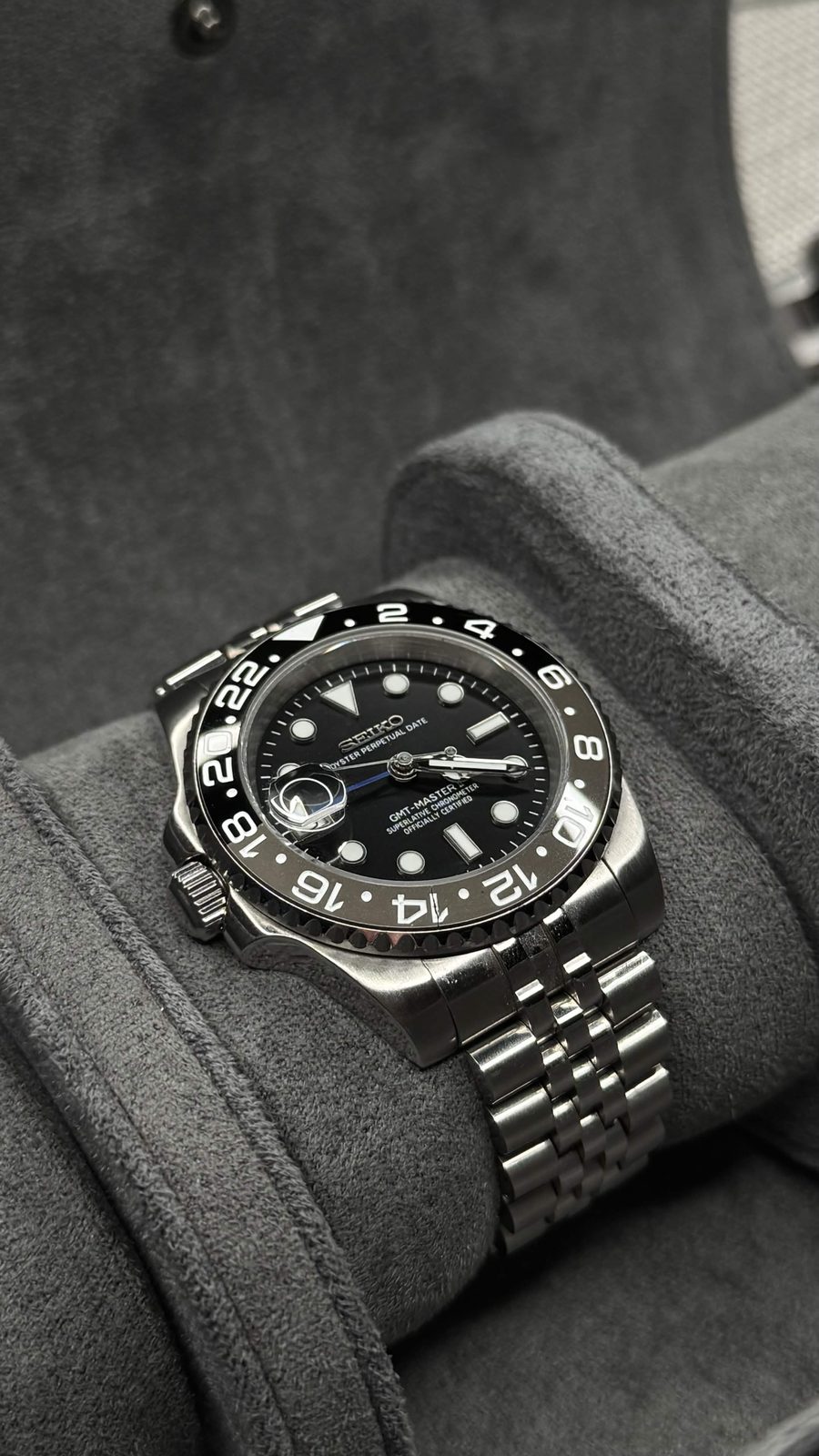 Seiko GMT mod with a black dial, black and grey bezel, and jubilee bracelet on a grey watch cushion